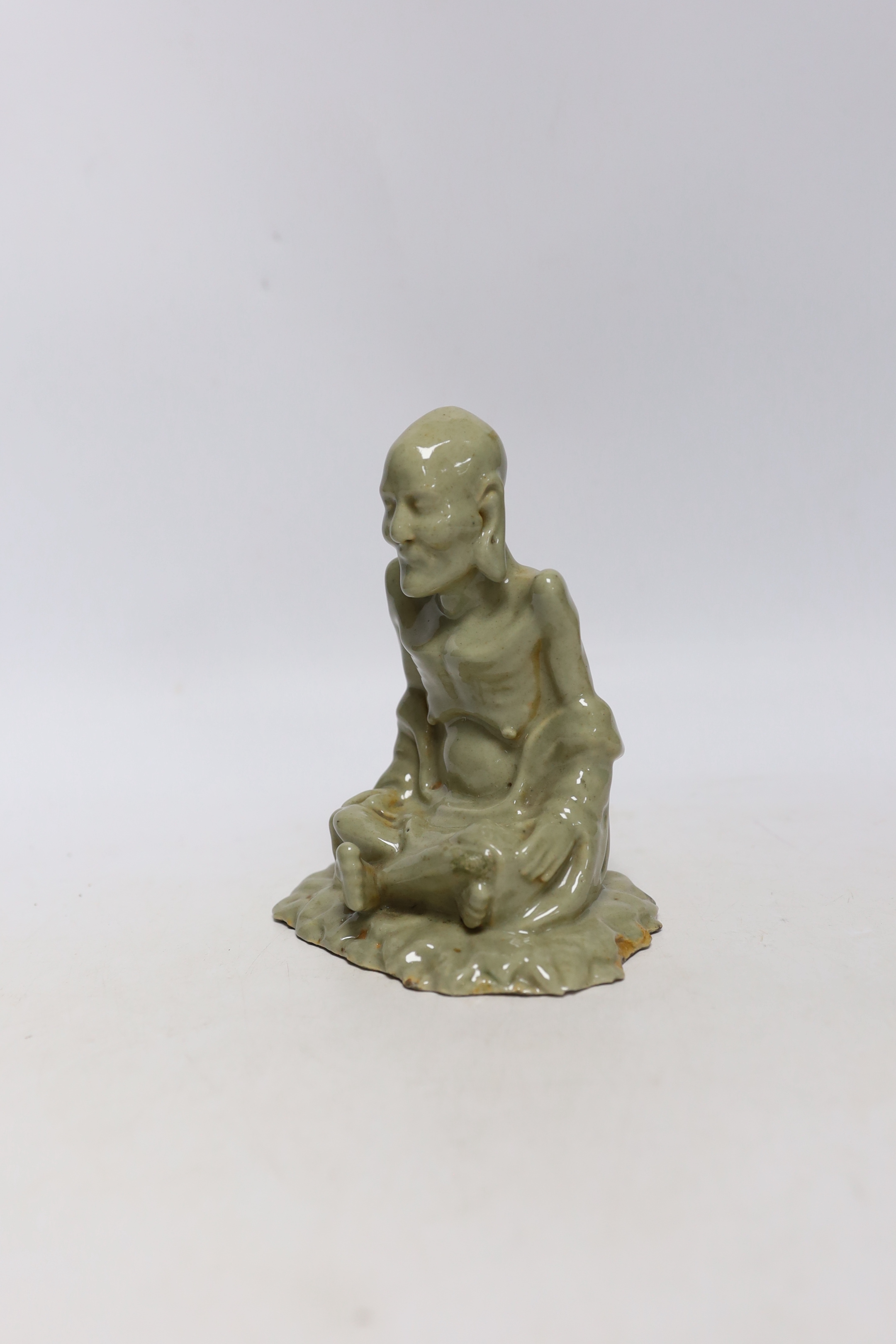 A Chinese celadon glazed figure of Laozi, 18th / 19th century, cross-legged and seated on leaves, 15cm high